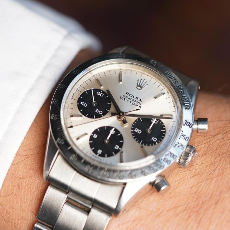 ساعة رولكس دايتونا Rolex Daytona ذات الرقم المرجعي 6239، مشغولة في علبة من الفولاذ بقطر 37 ملليمترًا وتزهو بعقارب ومؤشرات غير وضّاءة. 